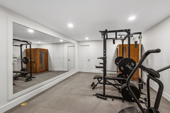 A home gym with a mirrored wall, weightlifting equipment, and a door.