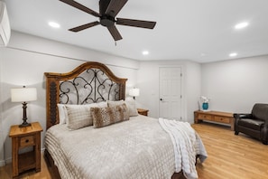 A bedroom with a bed, a ceiling fan, bedside lamps, a wooden nightstand, a door, and a chair.