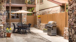 A patio with a table and chairs, a barbecue grill, and a stone wall.