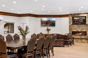 Un comedor con una gran mesa de madera, seis sillas y una chimenea de piedra con un televisor montado encima.