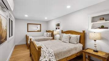 Une chambre à coucher avec deux lits en bois, une table de chevet avec une lampe, un miroir et une étagère avec des livres et une plante.