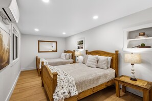 Une chambre à coucher avec deux lits en bois, une table de chevet avec une lampe, un miroir et une étagère avec des livres et une plante.