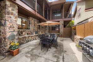 Un patio con paredes de piedra, una parrilla y mobiliario exterior.