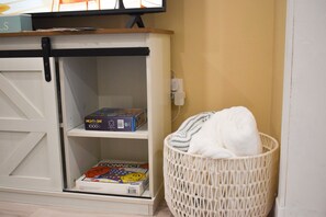A room with a white storage unit containing a puzzle box and a magazine. A white woven basket is placed against the wall.