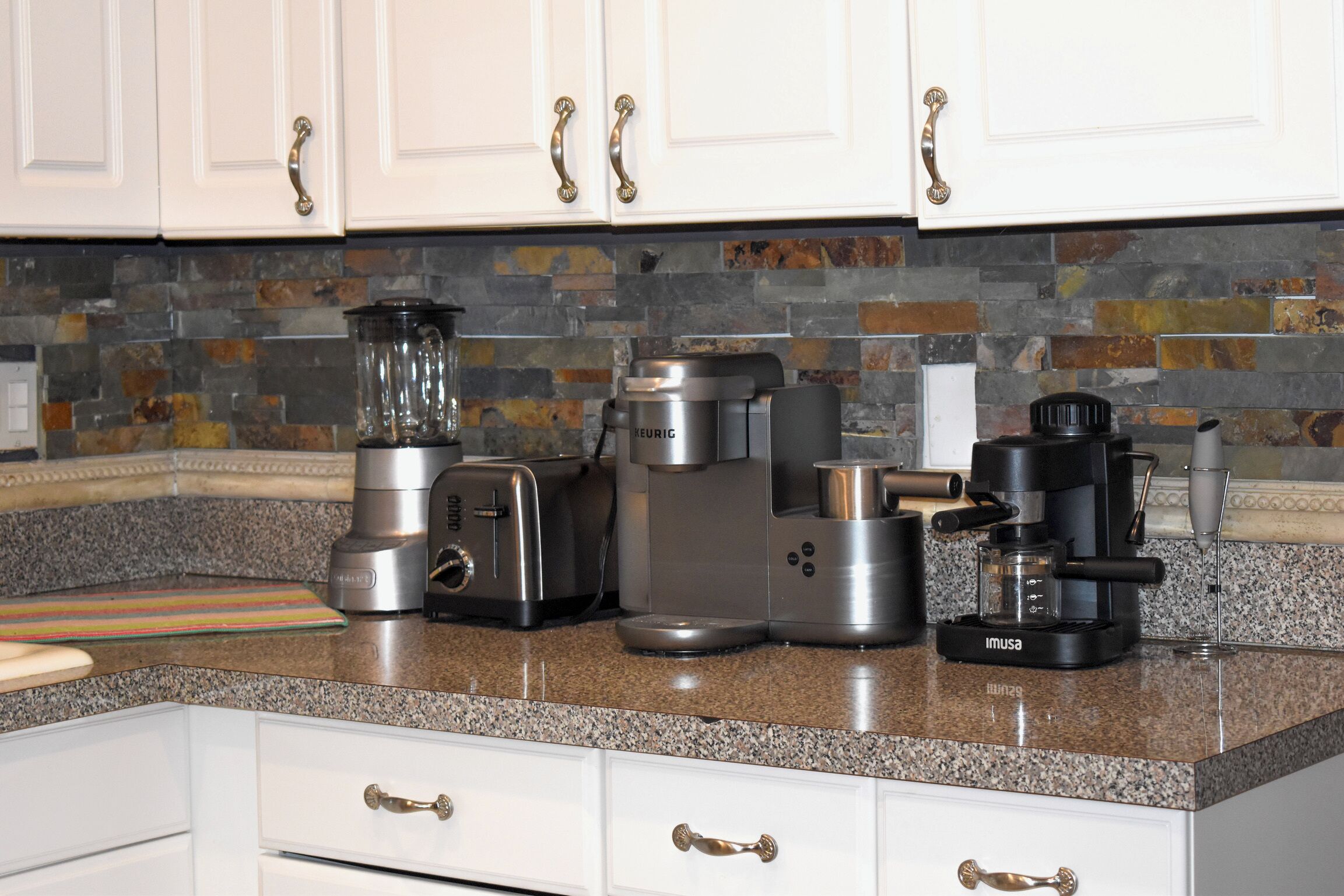 A kitchen with white cabinets, a granite countertop, and various appliances including a toaster, coffee maker, and blender.