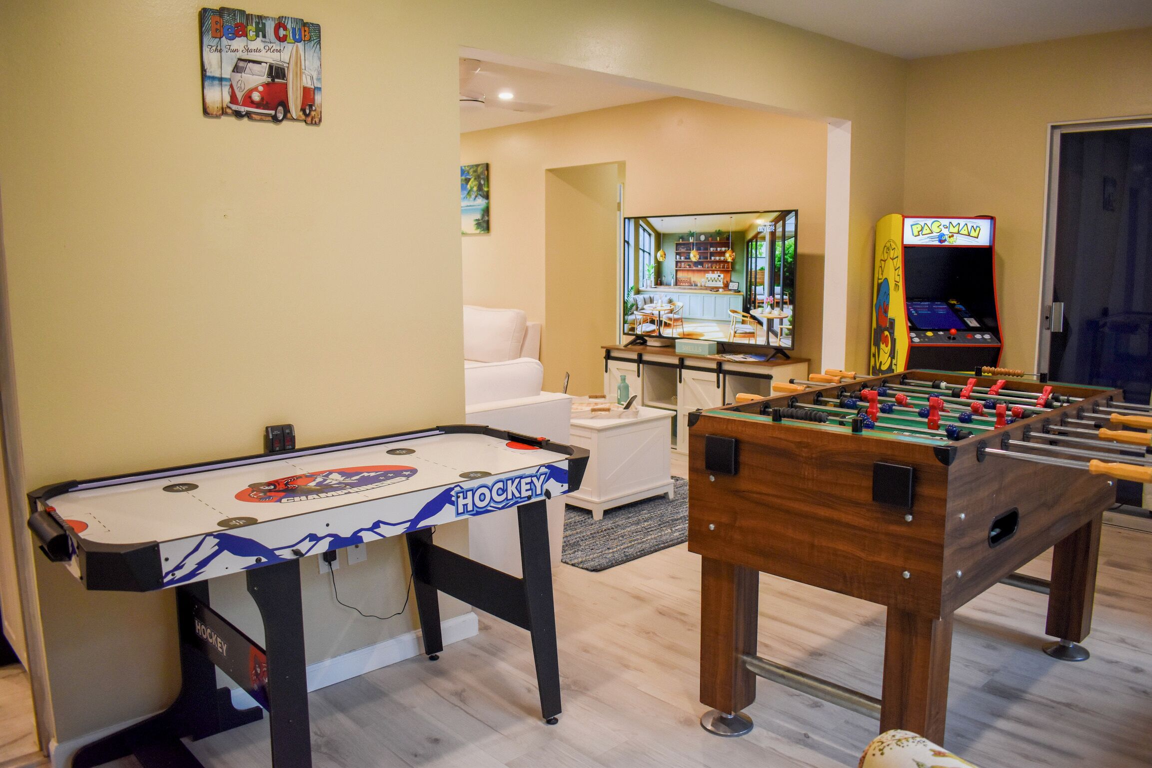 A room with a foosball table, a ping pong table, and a retro arcade machine.