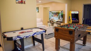 A room with a foosball table, a ping pong table, and a retro arcade machine.