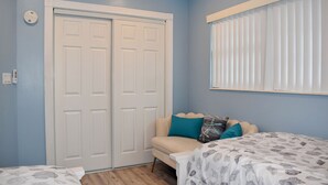 A bedroom with a double door, a window with blinds, a sofa, and a bed with a patterned bedspread.