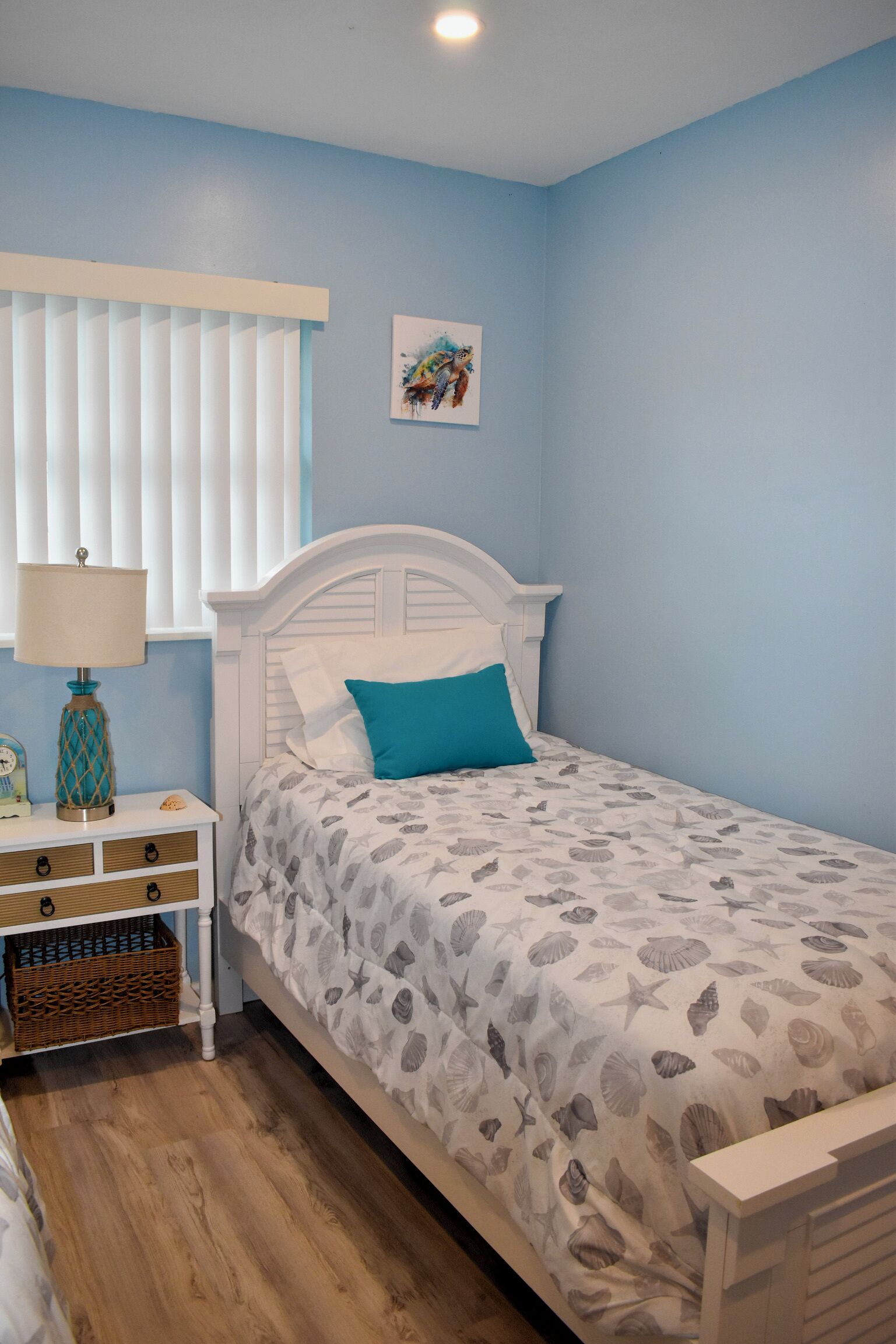 A bedroom with a bed, a nightstand, a lamp, and a wall with a painting.