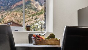 A dining area with a mountain view, a wicker basket with books, and a vase with white flowers.