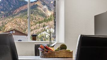 A dining area with a mountain view, a wicker basket with books, and a vase with white flowers.
