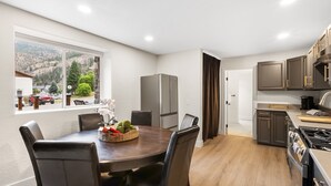 A modern kitchen with a dining area, large windows, and a view of the outdoors.