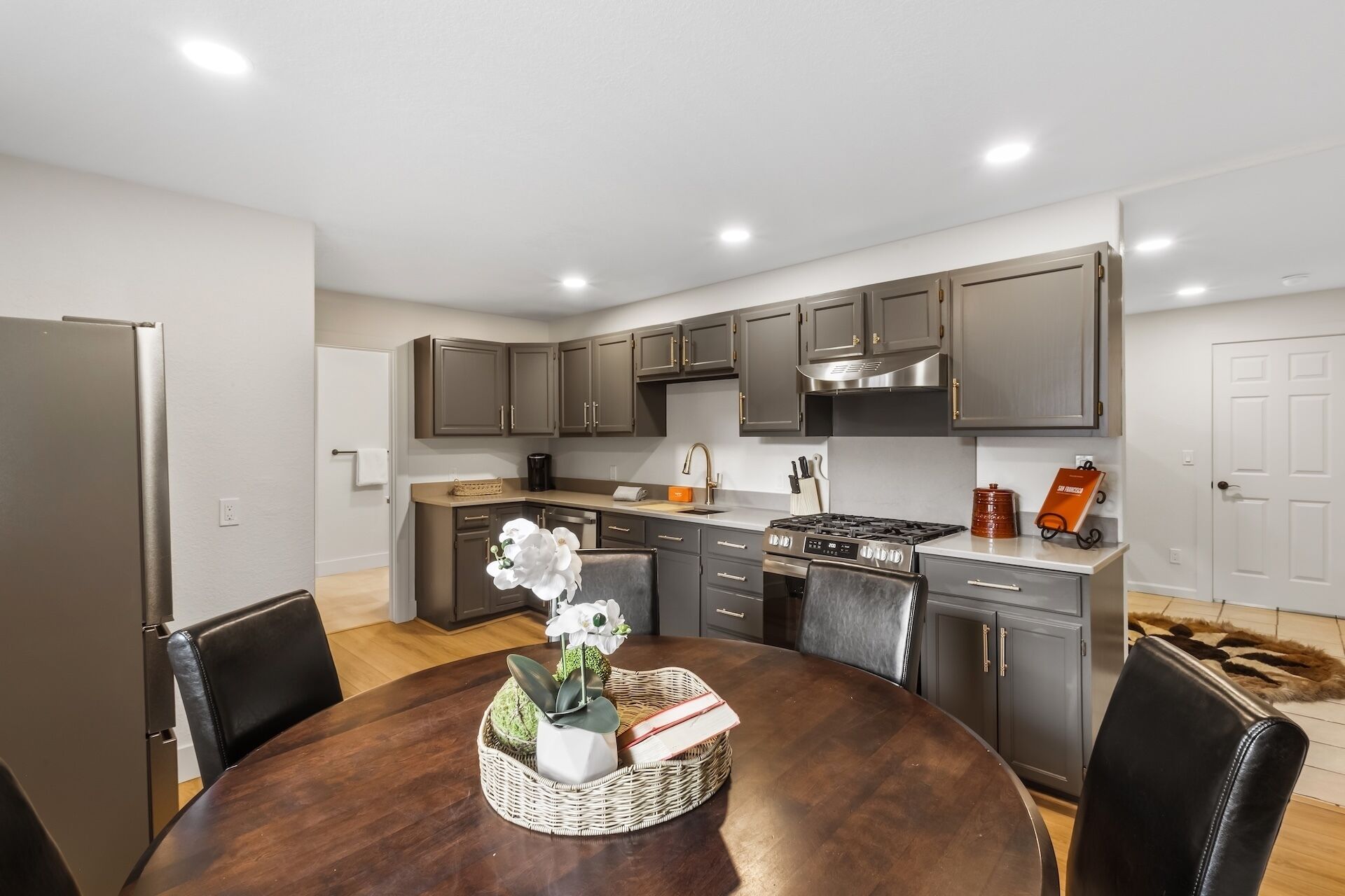 A modern kitchen with dark cabinets, a central island, and a dining area with a round table.