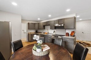 Una cocina moderna con armarios oscuros, una isla central y un comedor con una mesa redonda.