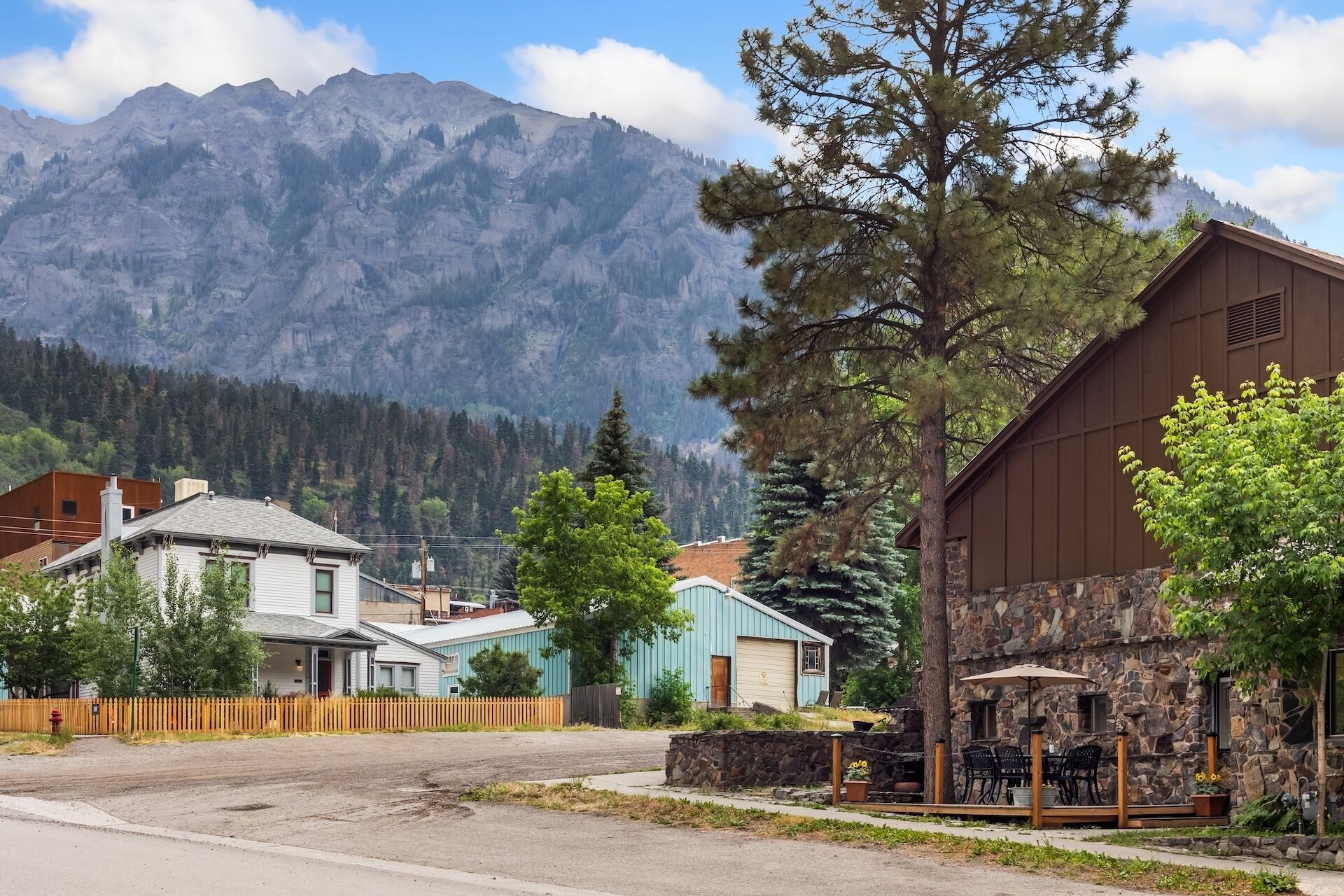 A mountain town with a stone building, a wooden fence, and houses in the foreground.