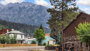 A mountain town with a stone building, a wooden fence, and houses in the foreground.