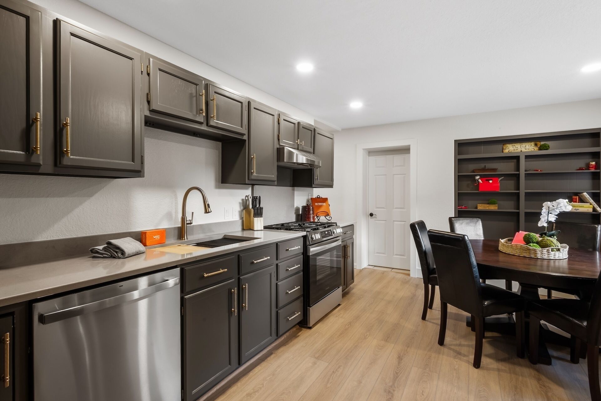 A modern kitchen with dark cabinets, stainless steel appliances, and a dining area with a table and chairs.