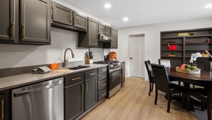 A modern kitchen with dark cabinets, stainless steel appliances, and a dining area with a table and chairs.