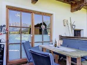 Ein Essbereich mit Tisch und Stühlen, Blick auf Berge durch große Fenster und einer rustikalen Holzbalkendecke.
