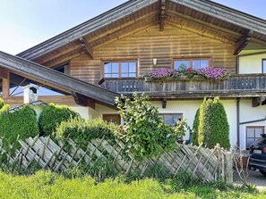 Eine zweistöckige Holzhütte mit Balkon, umgeben von gepflegten Hecken und einem Holzzaun.