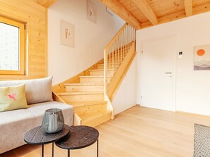 Eine Holztreppe führt zu einer zweiten Etage, ein Sofa mit Kissen, ein kleiner runder Tisch und eine Wand mit einem Bild.