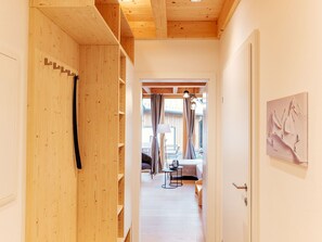 Ein Flur mit Holzwänden, einer Tür rechts und Blick in einen Raum mit Bett, Vorhängen und einer Lampe.