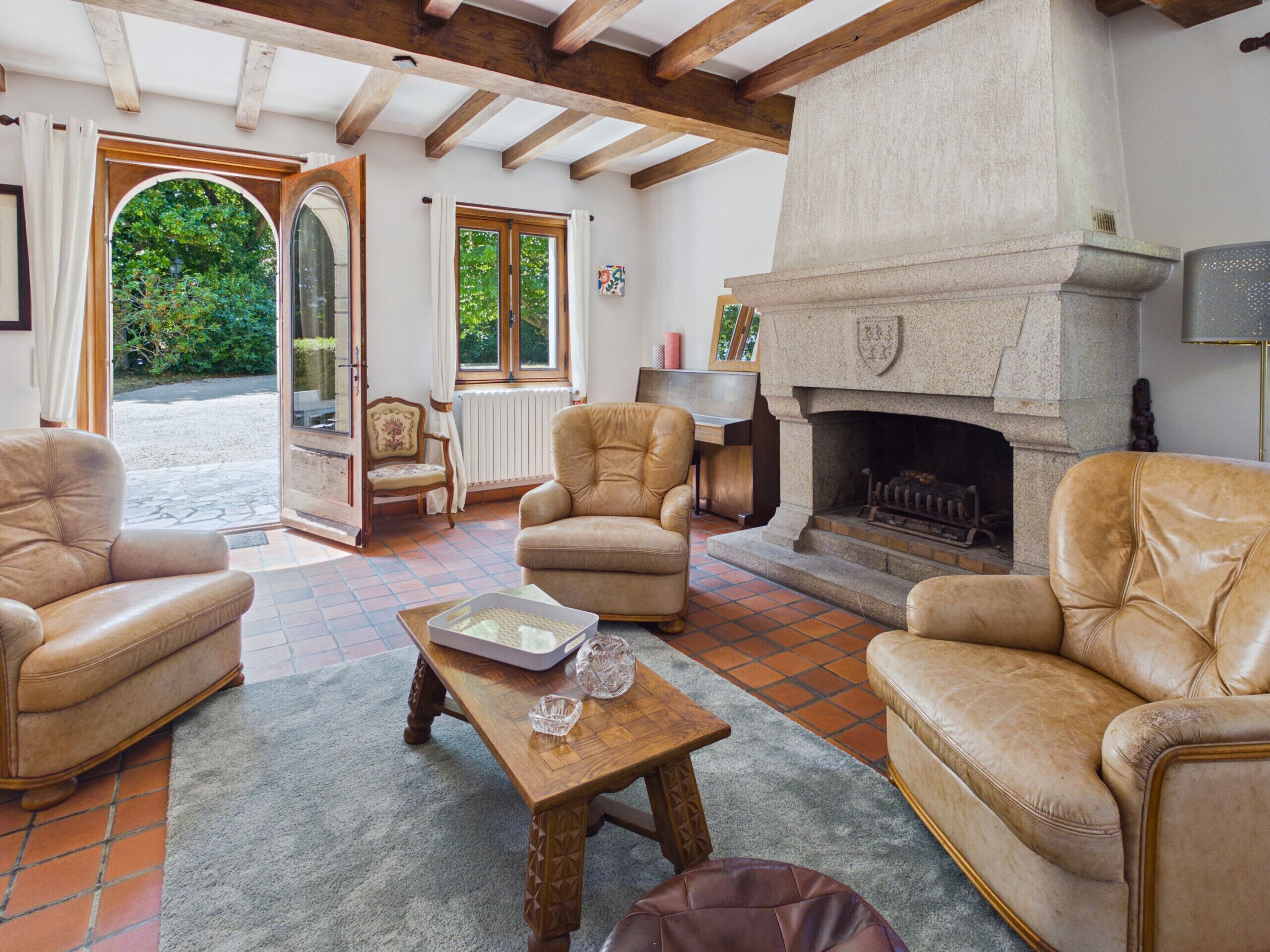 A cozy living room with leather sofas, a fireplace, and a view of the garden through a large window.