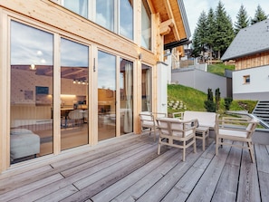 A wooden deck with outdoor furniture, large sliding glass doors leading to an interior space, and a view of a residential area with trees and a building in the background. - Beautiful private villa for 8 people with TV, terrace and pets allowed (Lachtal)