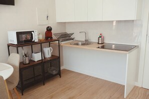 Cocina compacta con microondas, hervidor, tostadora y un lavamanos pequeño.