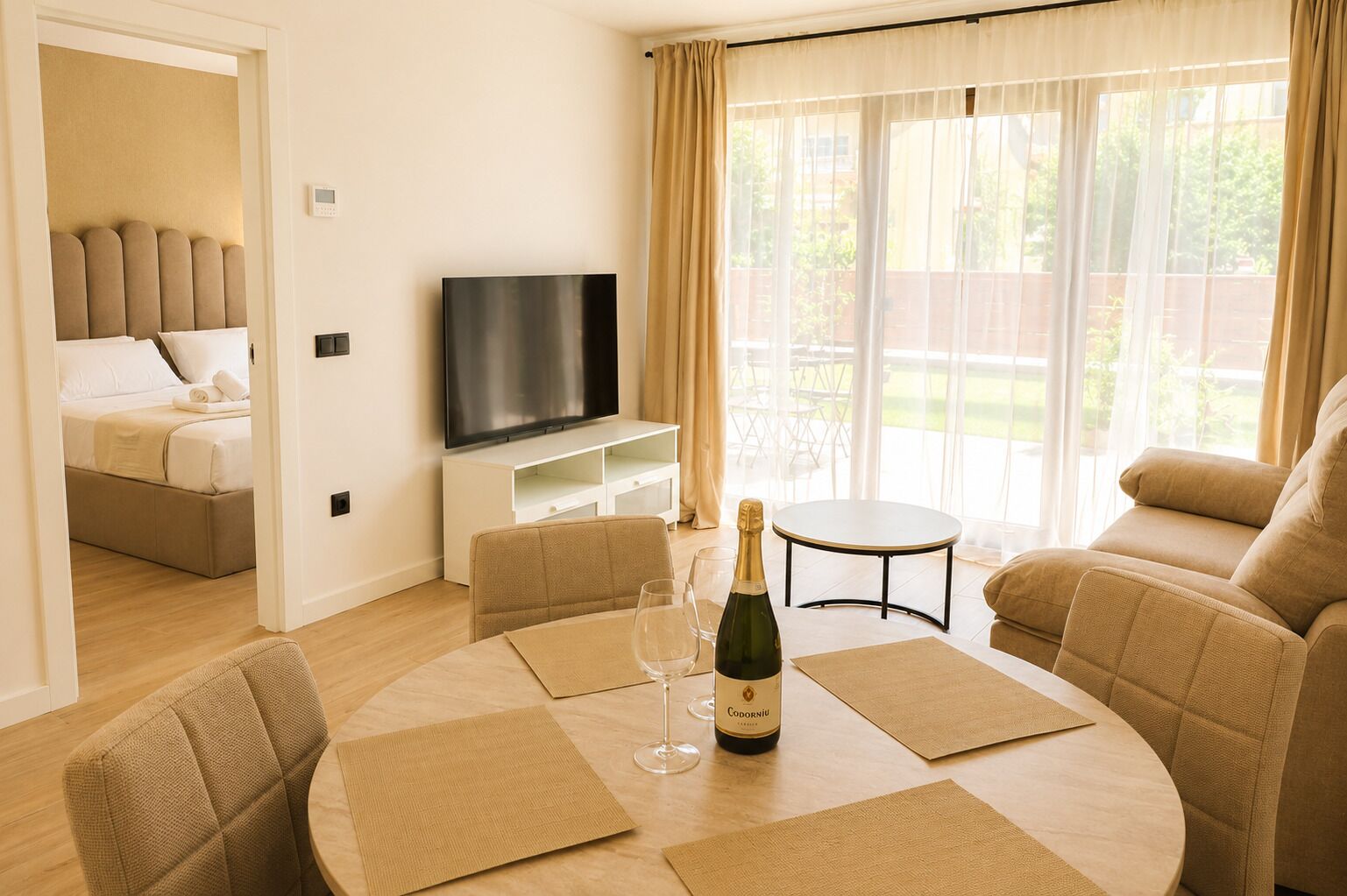 A modern living room with a flat-screen TV, a dining table with placemats, a bottle of wine, and a sofa.