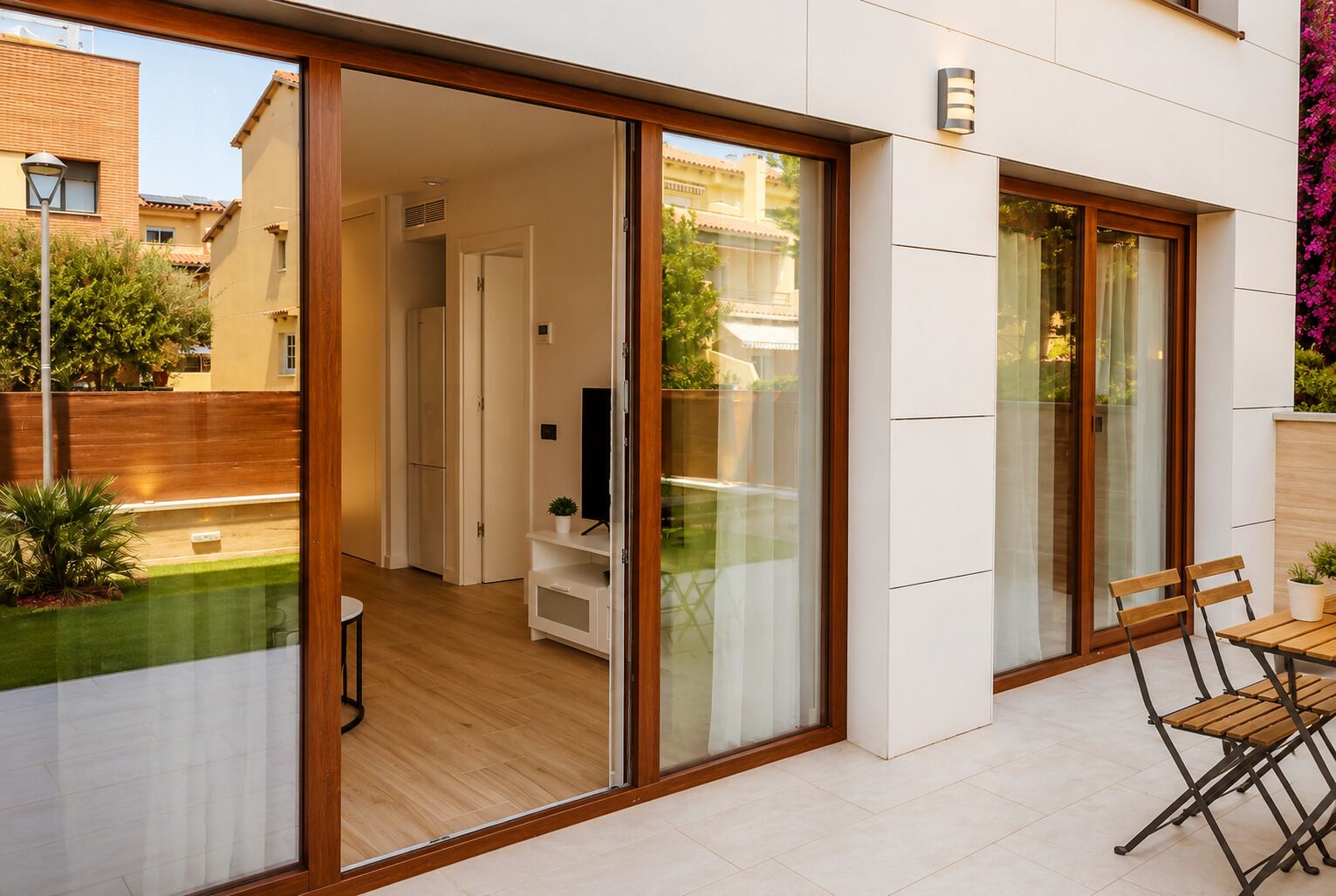 A modern residential property with a sliding glass door leading to a living area, a small balcony with a table and chairs, and a view of the surrounding neighborhood.