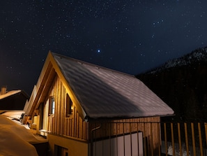 Eine Holzhütte mit geneigtem Dach, einem Fenster und einer Tür vor einem sternenübersäten Nachthimmel.
