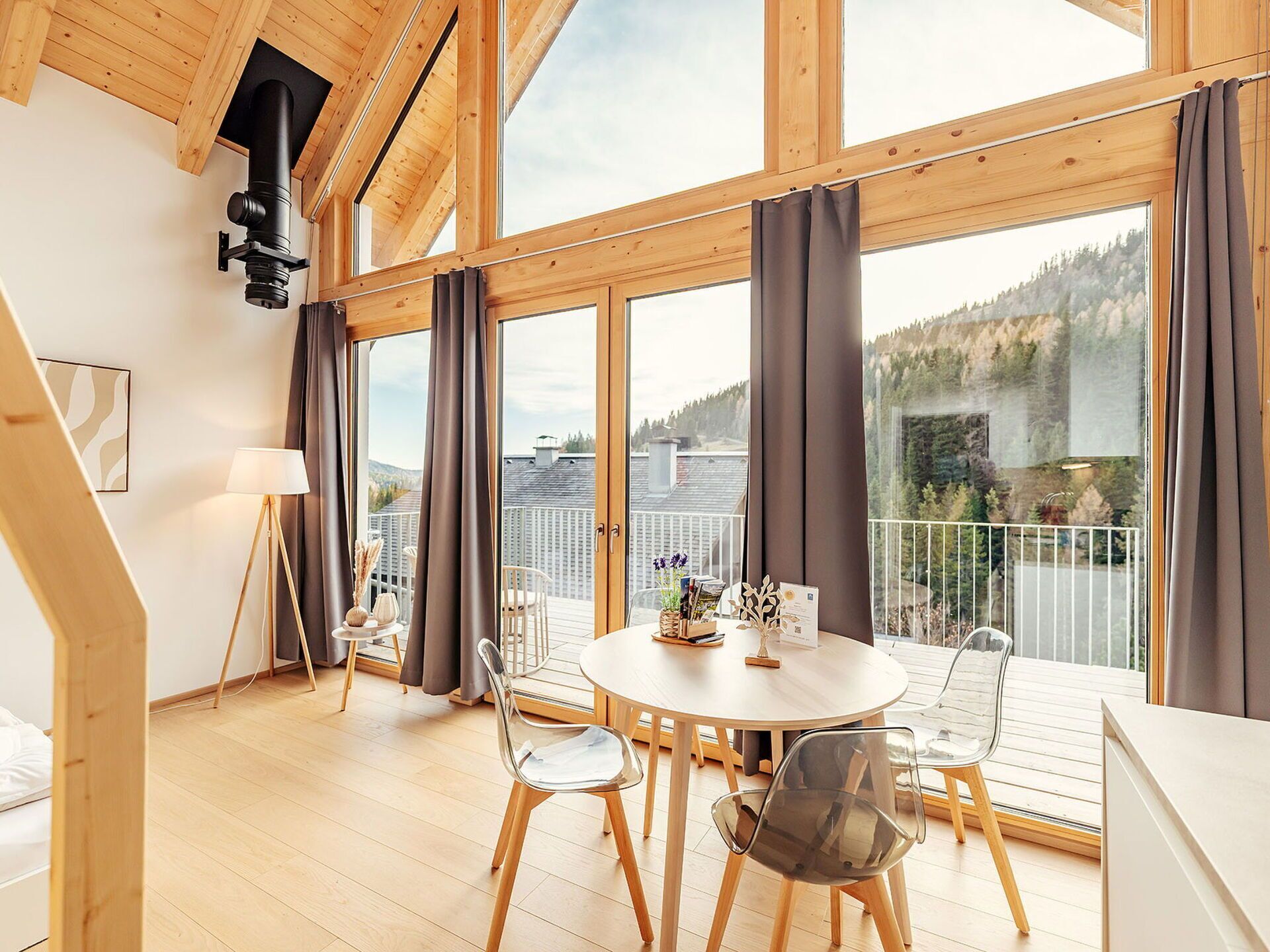 A spacious room with a large window, wooden ceiling beams, a round dining table, and modern chairs.