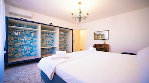 Ein Schlafzimmer mit Bett, einem Kleiderschrank mit floralem Wandpapier, einer Chandelüster, einem Spiegel und einer Kommode.