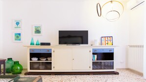 A living room with a television on a cabinet, decorative items on the wall, and a radiator. - Solemar Sicilia - Stella Marina (Santa Flavia)