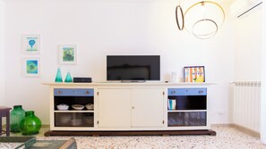 Ein Wohnzimmer mit Fernseher auf einem Schrank, Dekoration an der Wand und einer Heizung.