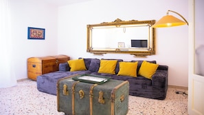 A room with a sofa, a large mirror, a lamp, a suitcase, and a small wooden cabinet. - Solemar Sicilia - Stella Marina (Santa Flavia)