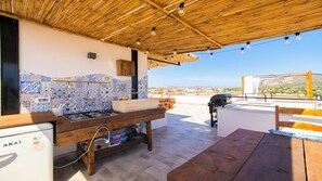 An outdoor kitchen area with a gas stove, wooden table, and a view of the landscape. - Solemar Sicilia - Stella Marina (Santa Flavia)