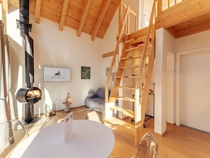 Um interior moderno com teto de madeira, lareira, escada, sofá e mesa.