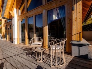 Eine Holzterrasse mit zwei Korbstühlen und einem Tisch, mit Blick auf ein Gebäude mit großen Fenstern.