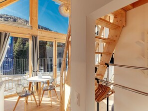 Ein modernes Interieur mit einer Holztreppe, einem Balkon mit Tisch und Stühlen und Blick ins Freie.