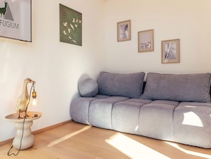 A modern living room with a grey sofa, a small side table with a decorative lamp, and wall art. - Stunning  villa for 2 people with WIFI, TV, terrace and pets allowed (Lachtal)
