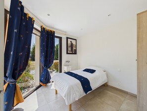 Ein Schlafzimmer mit einem Bett, einem Nachttisch, einem Fenster mit Vorhängen und einem gerahmten Bild an der Wand.