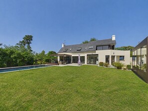 Ein modernes, zweistöckiges Haus mit Swimmingpool, überdachter Terrasse und gepflegtem Rasen.