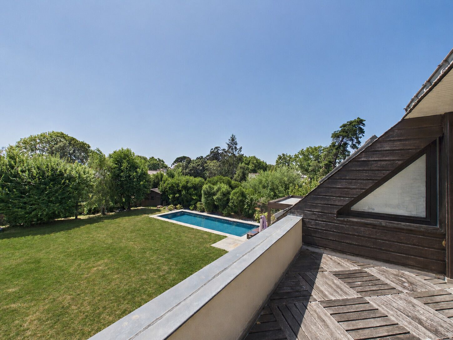 Un giardino con piscina, terrazza in legno e una casa con tetto spiovente.