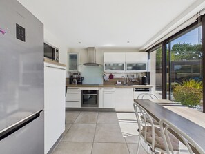 A modern kitchen with stainless steel appliances, a dining area with a wooden table and chairs, and a large window offering a view of the outdoors. - Modern house for 7 with heated pool (Arradon)