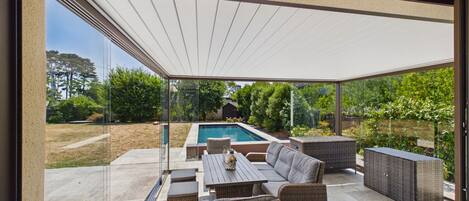 A covered outdoor patio with a pool, wicker furniture, and a view of a backyard.