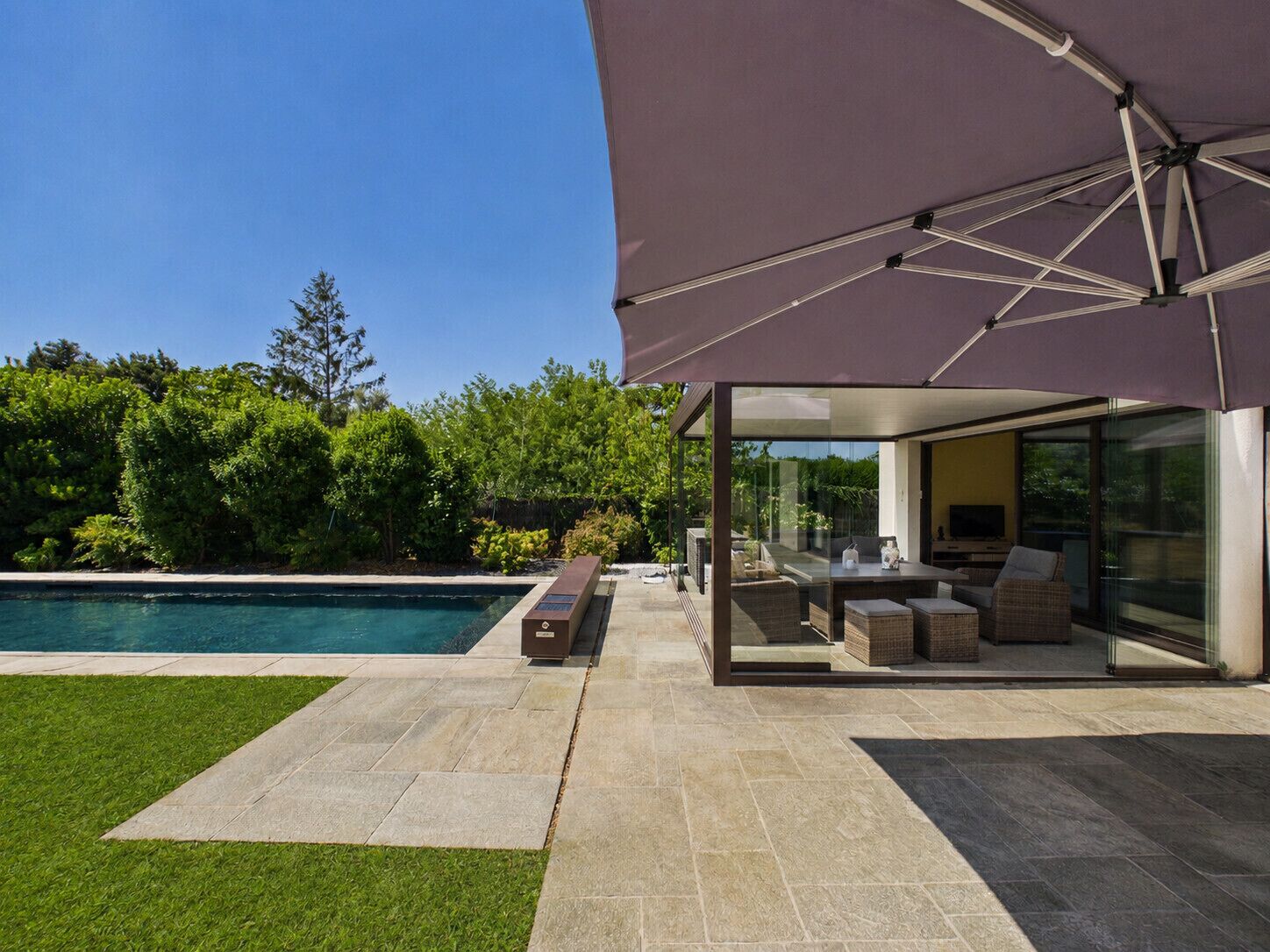 Eine moderne Außenpatio mit Pool, Sitzgelegenheit und einem überdachten Bereich mit großem Sonnenschirm.