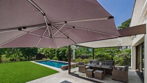 A covered outdoor seating area with a pool in the background. - Modern house for 7 with heated pool (Arradon)