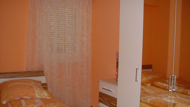 Quarto com duas camas, um guarda-roupa e uma janela com cortina.